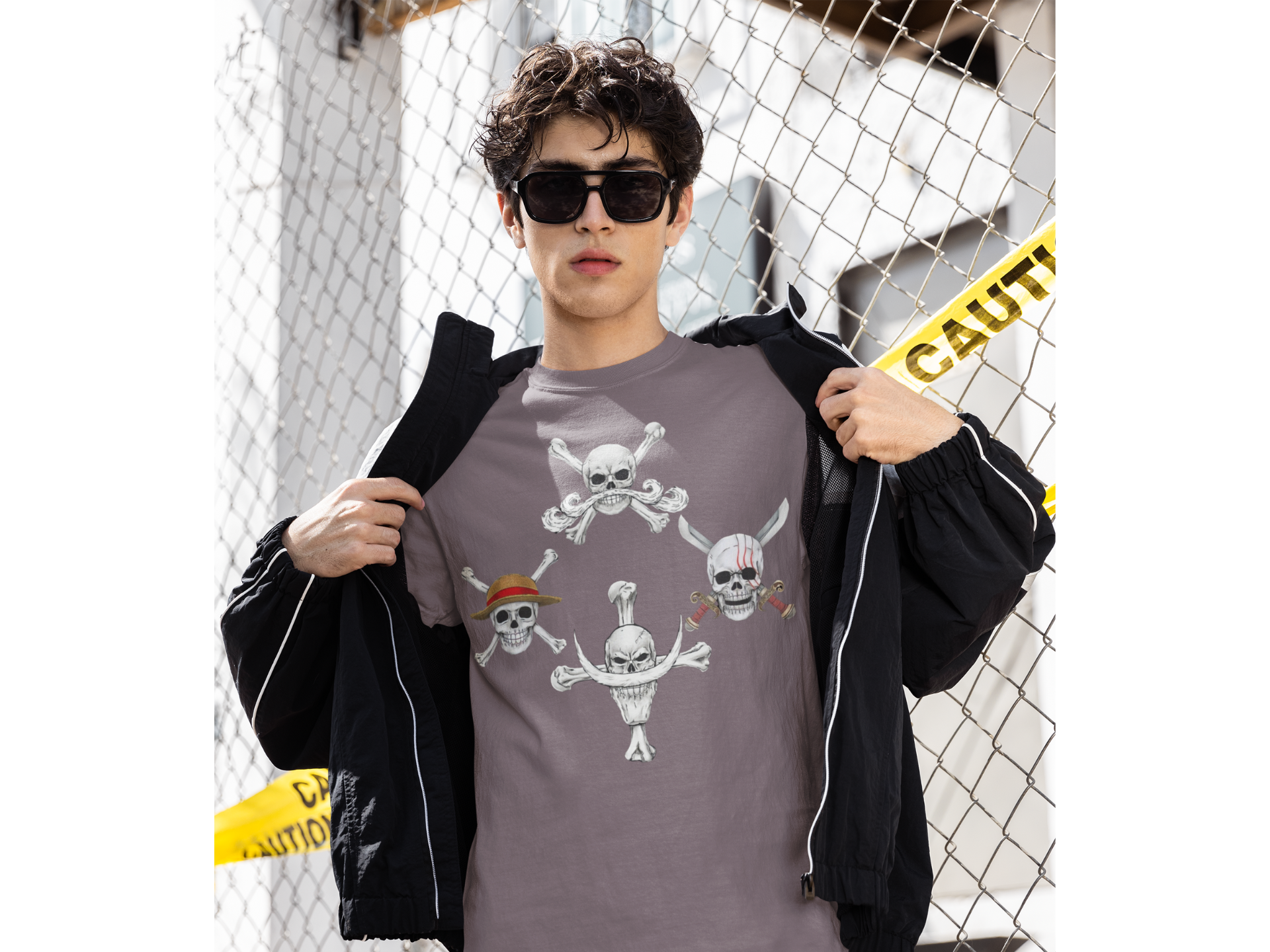 Person wearing a gray t-shirt with skull and crossbones design, standing in front of a chain-link fence.